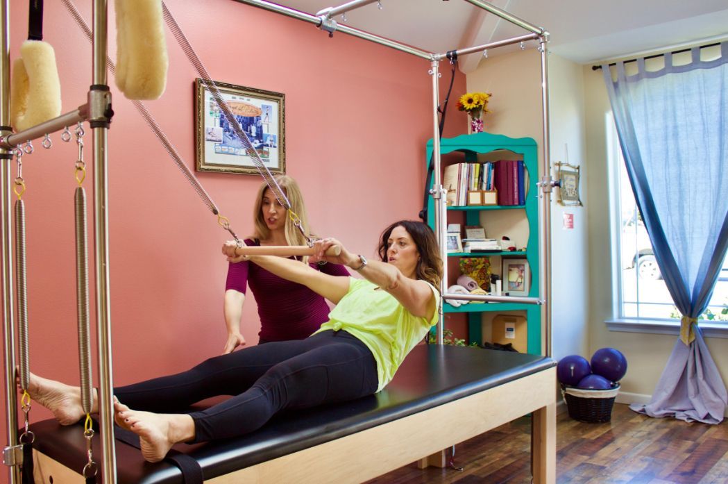 a woman is laying on a pilates machine while a woman stands behind her .