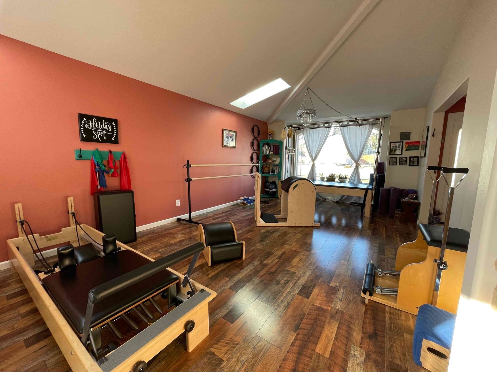 Pilates studio with equipment on a wood floor, coral walls, and natural light.