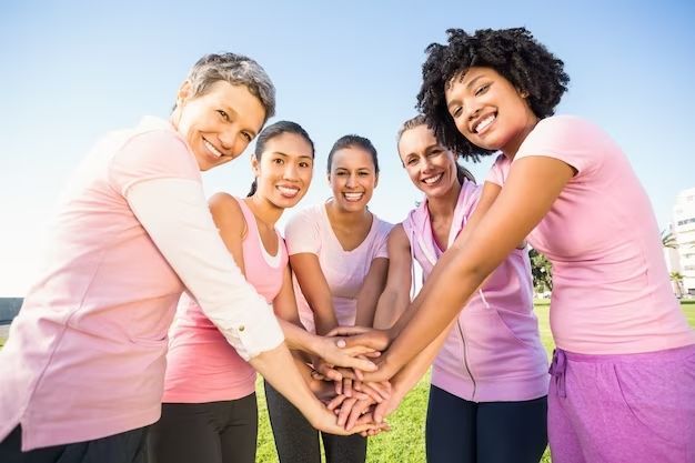 A group of women in pink shirts are putting their hands together.