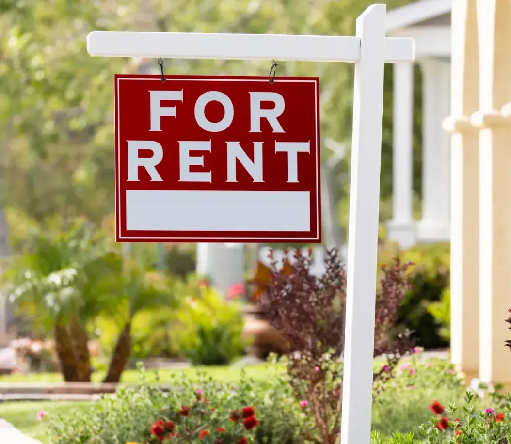 A red for rent sign is hanging in front of a house.