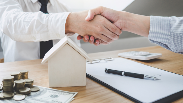 A man is shaking hands with another man in front of a model house.