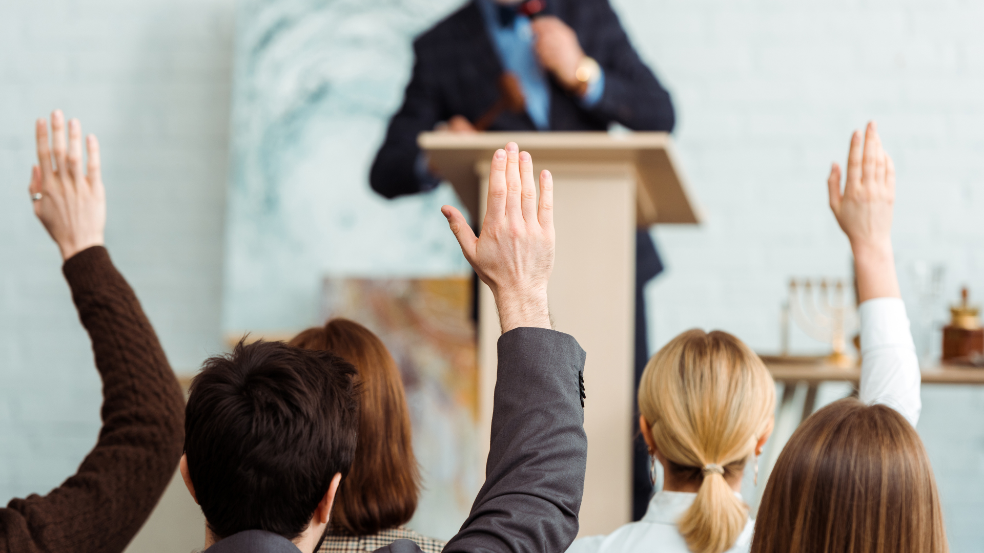 A group of people are raising their hands in a classroom to answer a question.