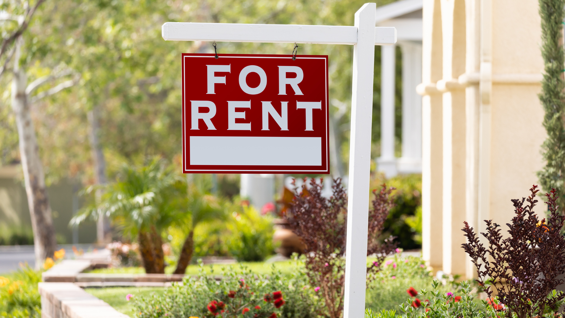A red for rent sign is hanging in front of a house.
