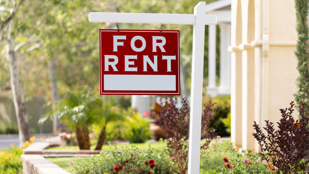 A red for rent sign is hanging in front of a house.