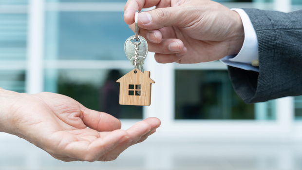 A man is handing a house key to another man.