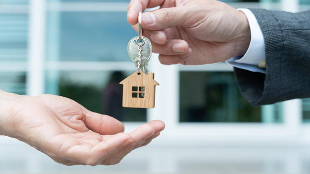 A man is handing a house key to another man.