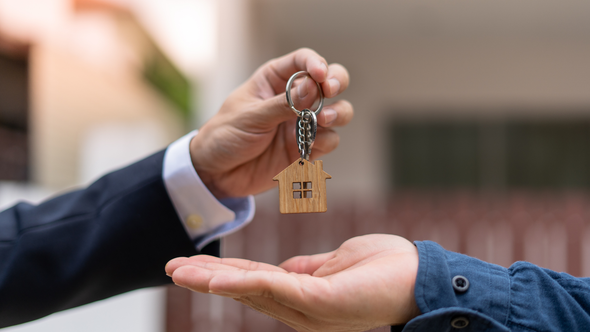 A man is handing a house key to another man.