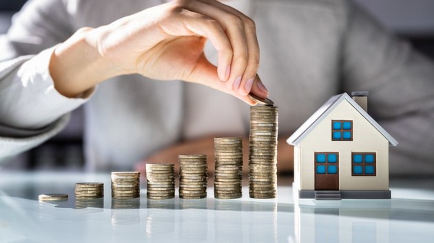 A person is putting coins into a stack next to a model house.