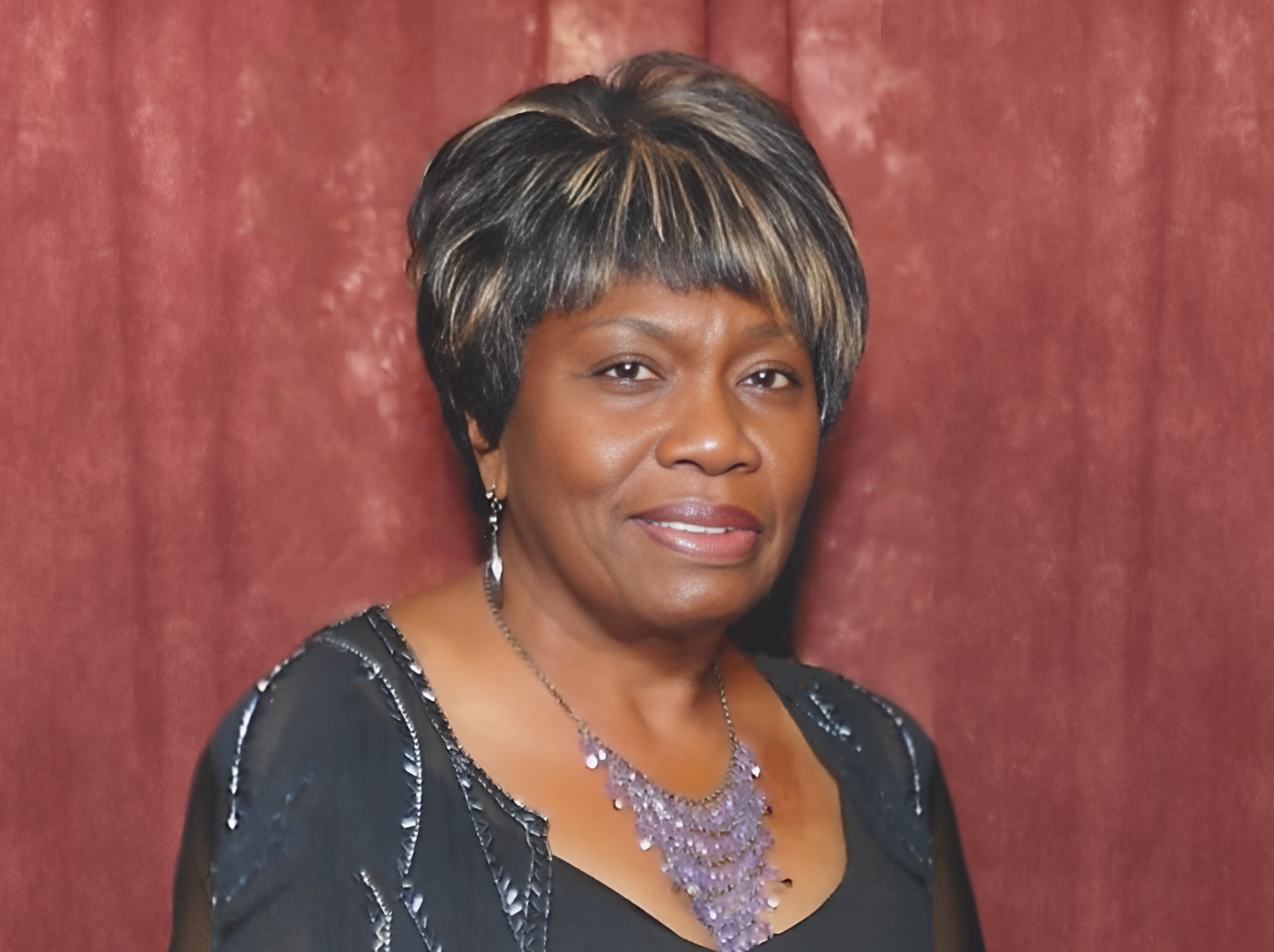 A woman wearing a black dress and a purple necklace
