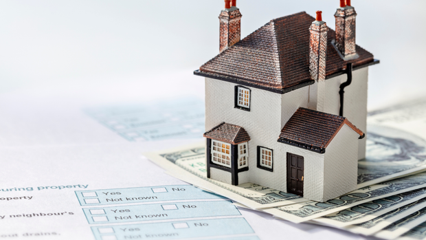 A model house is sitting on top of a pile of money.