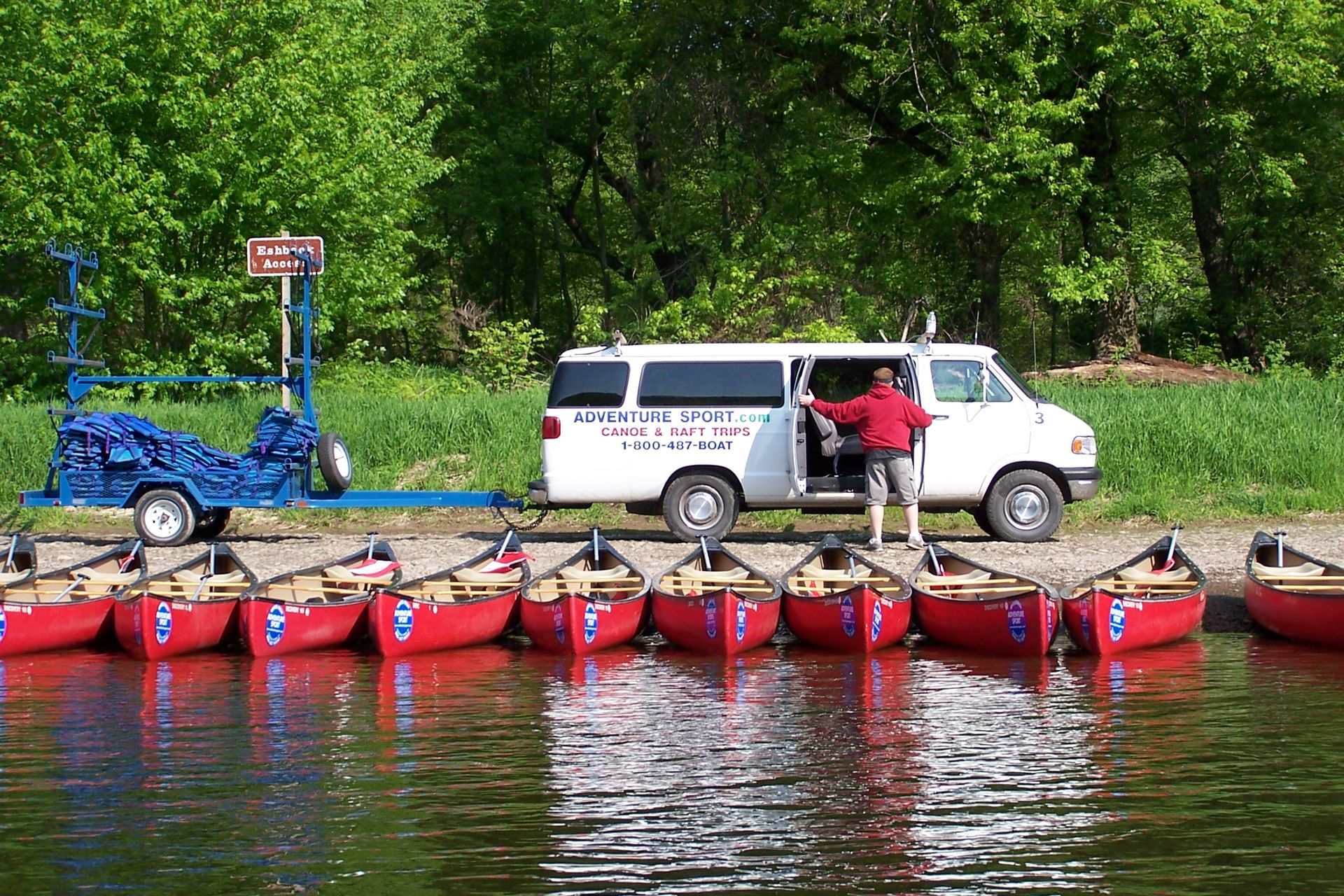 A white van is pulling a trailer full of red adventure sports canoes