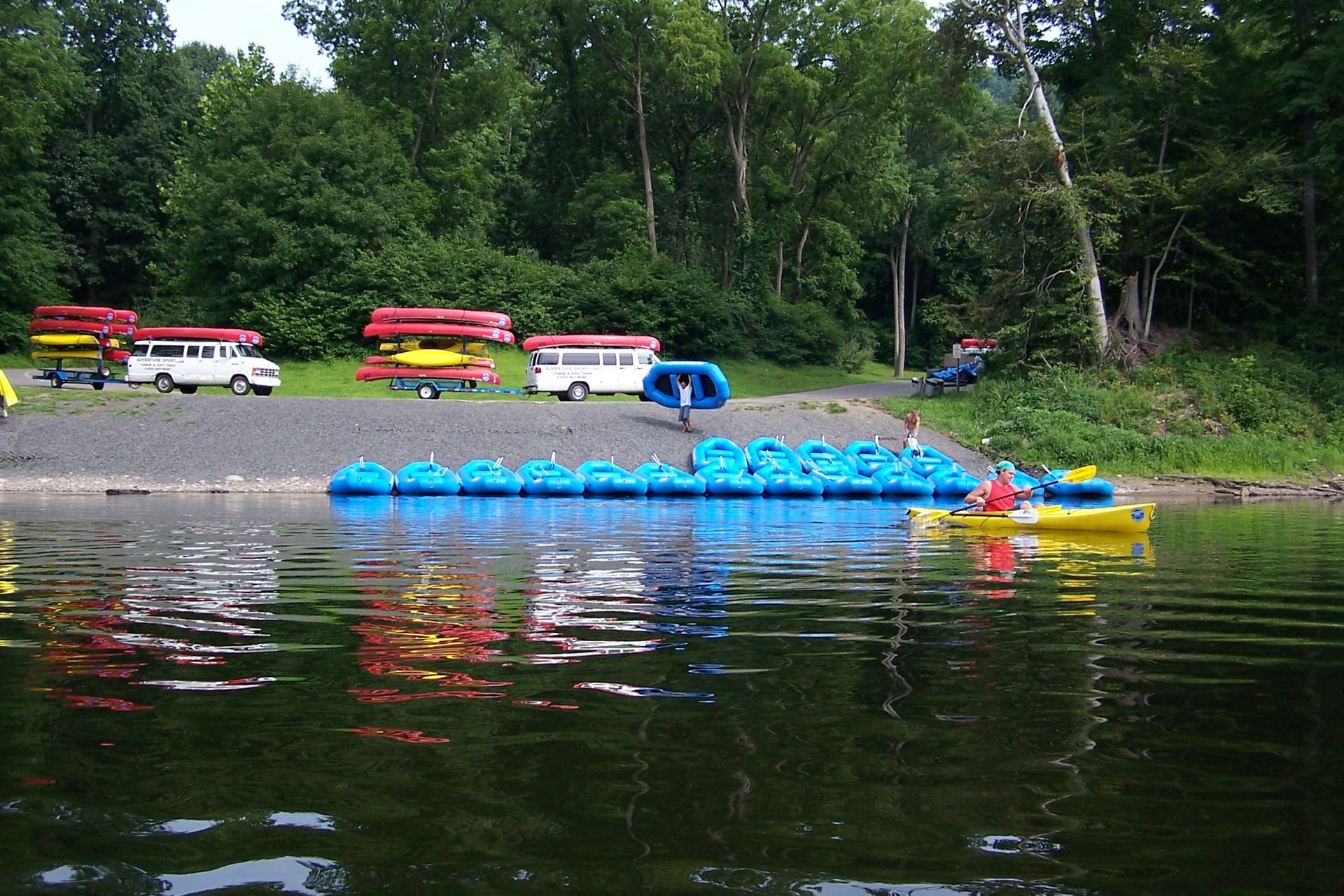 A row of adventure sports kayaks are lined up on the shore of a lake