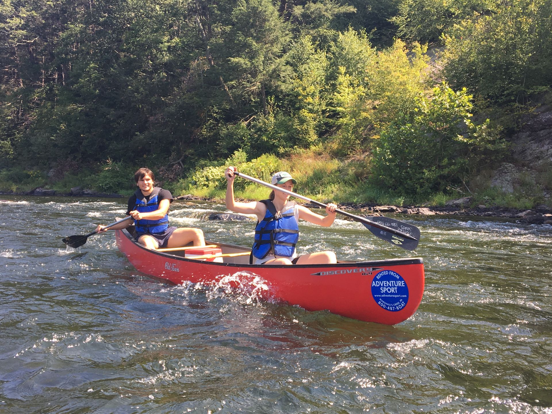 Two people are paddling a red adventure sports canoe on a river