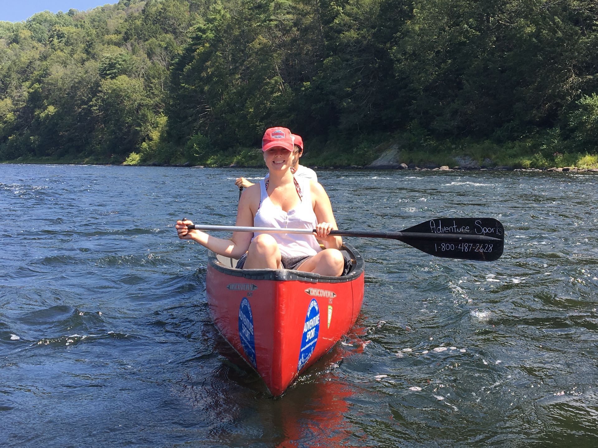 A woman is paddling a red adventure sports canoe on a river.