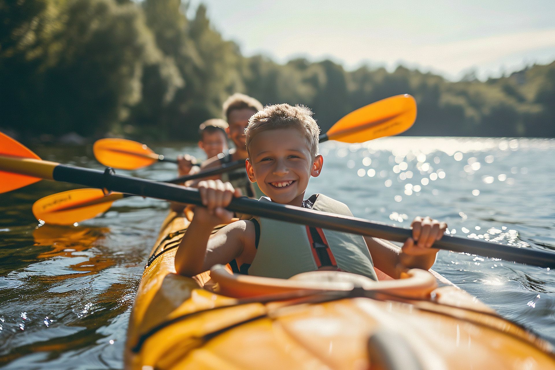 Two people kayaking on a sunlit lake, smiling in orange kayaks with paddles raised.