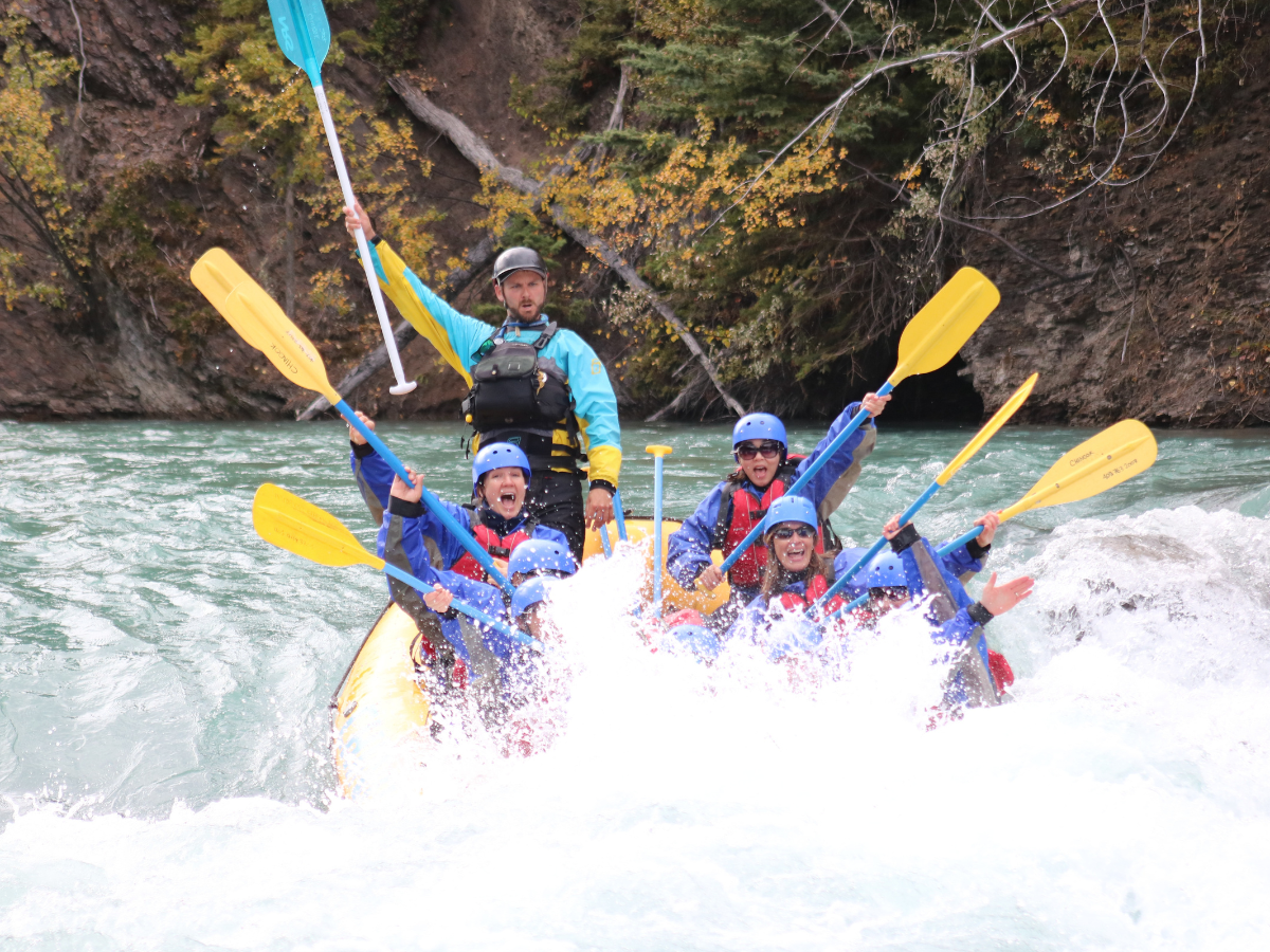 A group of people white water rafting, raising paddles in celebration through splashing rapids. A group of people white water rafting, raising paddles in celebration through splashing rapids.