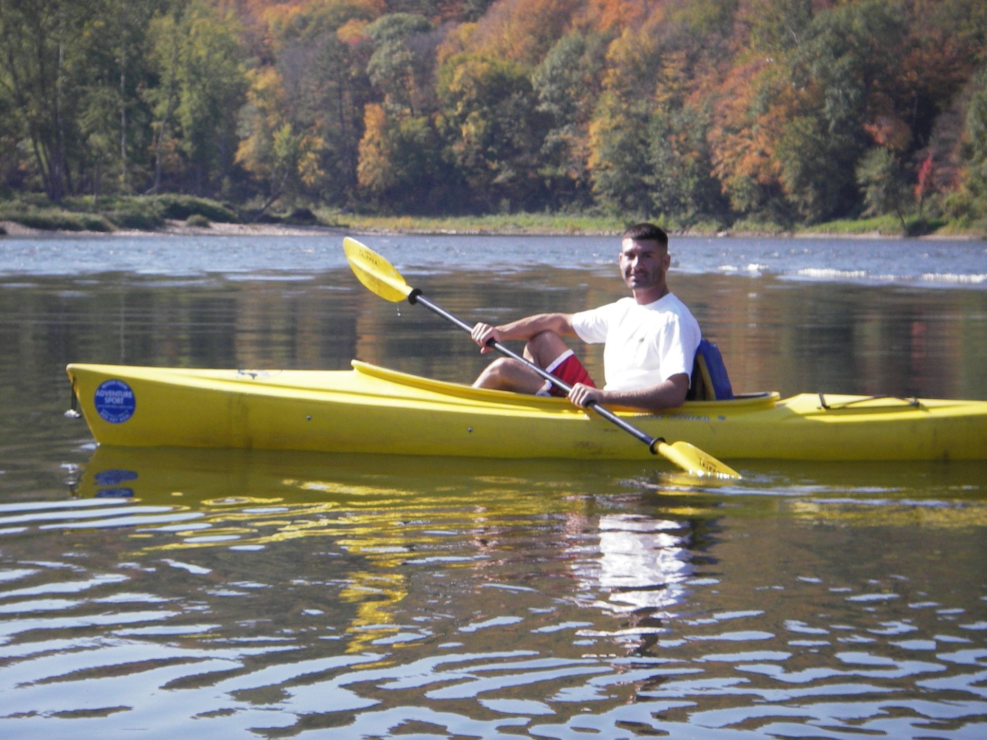 A man is paddling a yellow adventure sports kayak on a lake