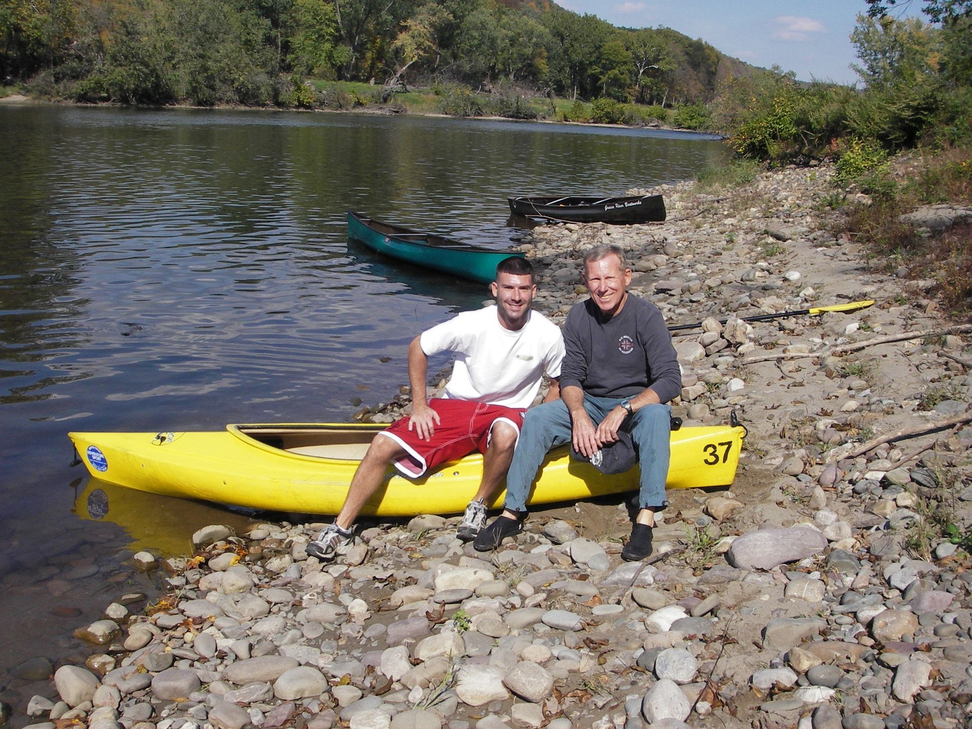 Two men sit on a yellow adventure sports kayak with the number 37 on it