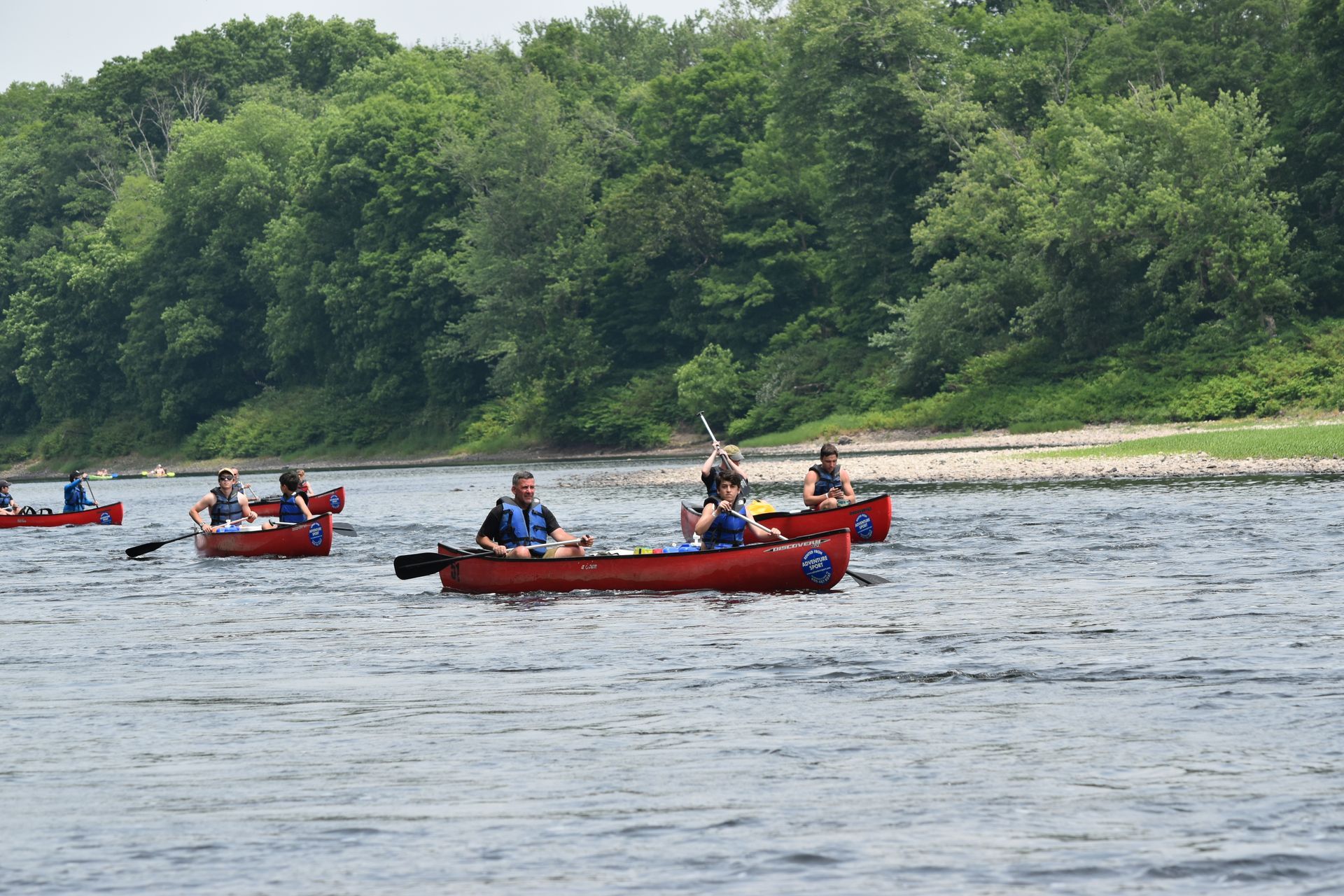 A group of people are rowing adventure sports canoes down a river.