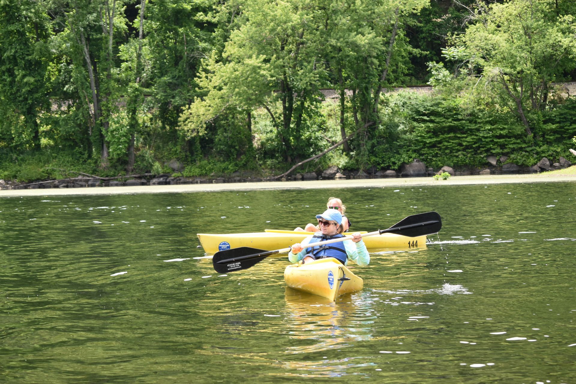 A man and a child are paddling adventure sports kayaks on a lake.