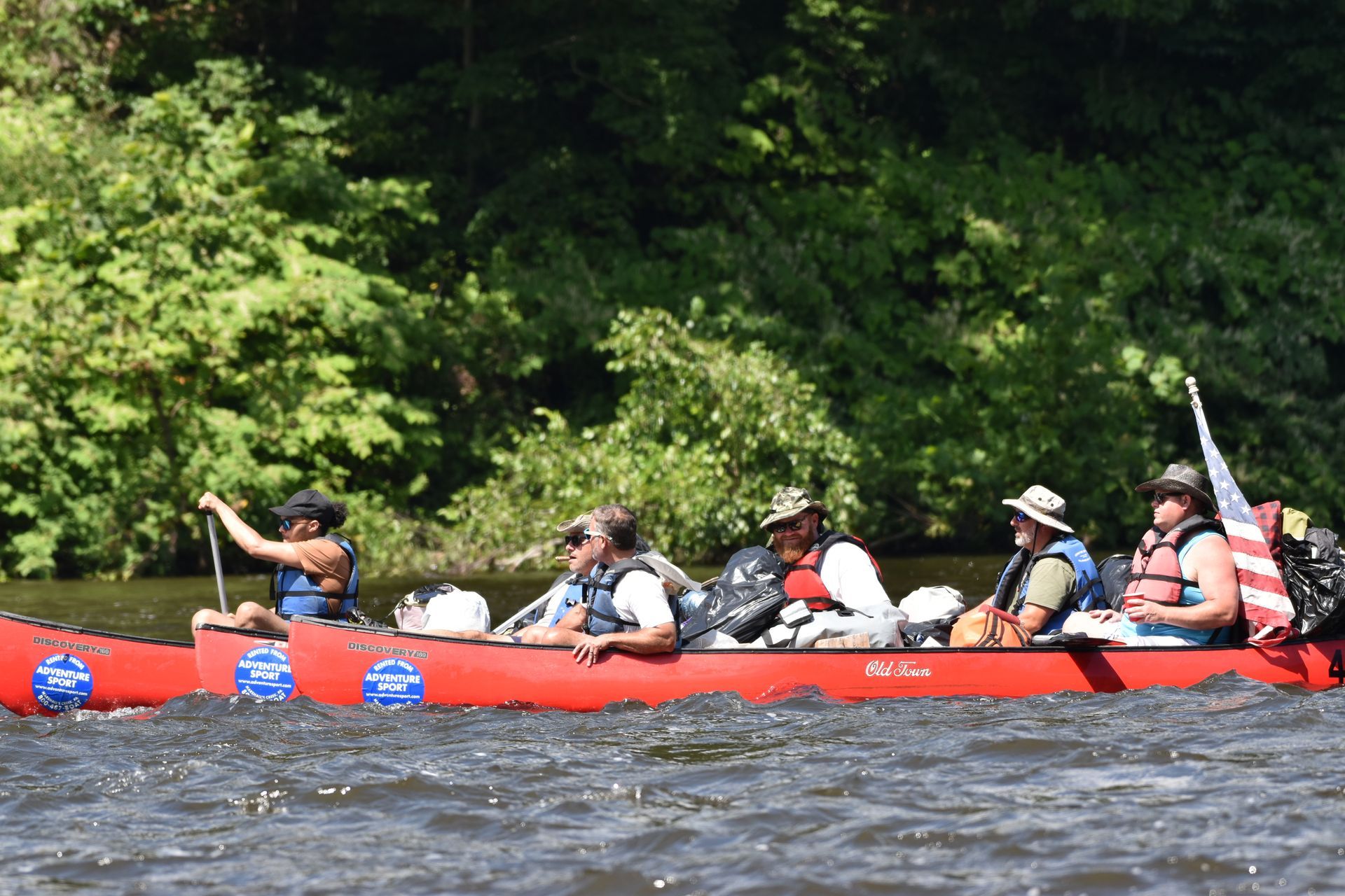 A group of people are in a red adventure sports canoe on a river.