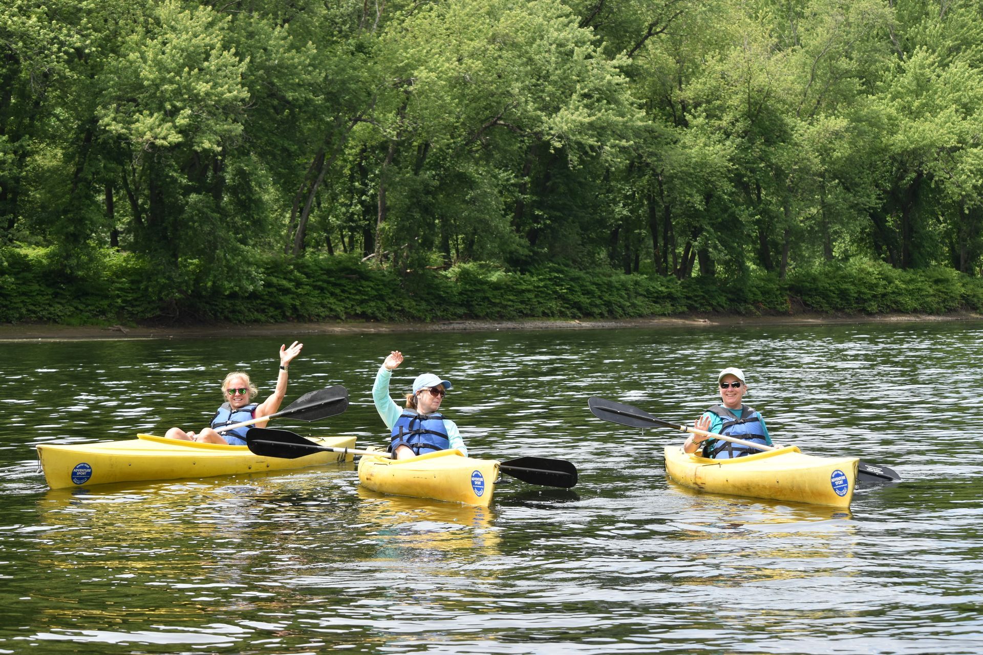 Three people are rowing adventure sports kayaks on a lake.