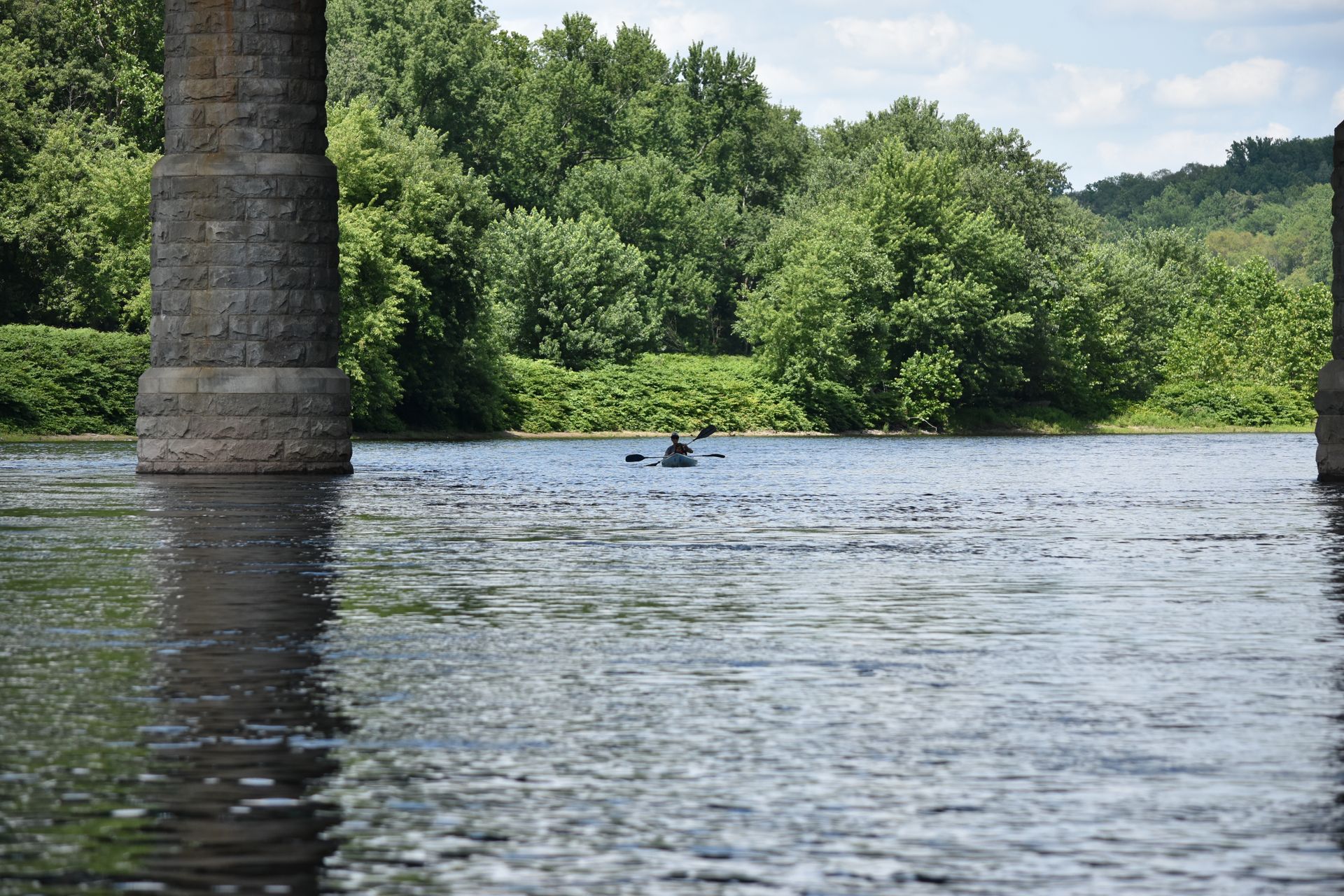 A person is paddling an adventure sports kayak under a bridge