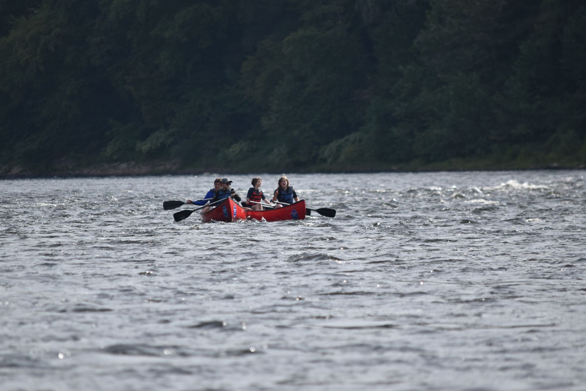 A group of people are paddling a red adventure sports canoe on a lake.
