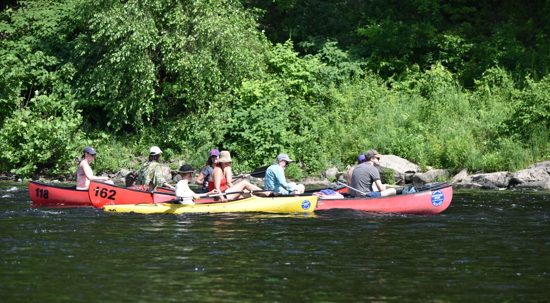A row of adventure sports rafts are lined up on the shore of a river.