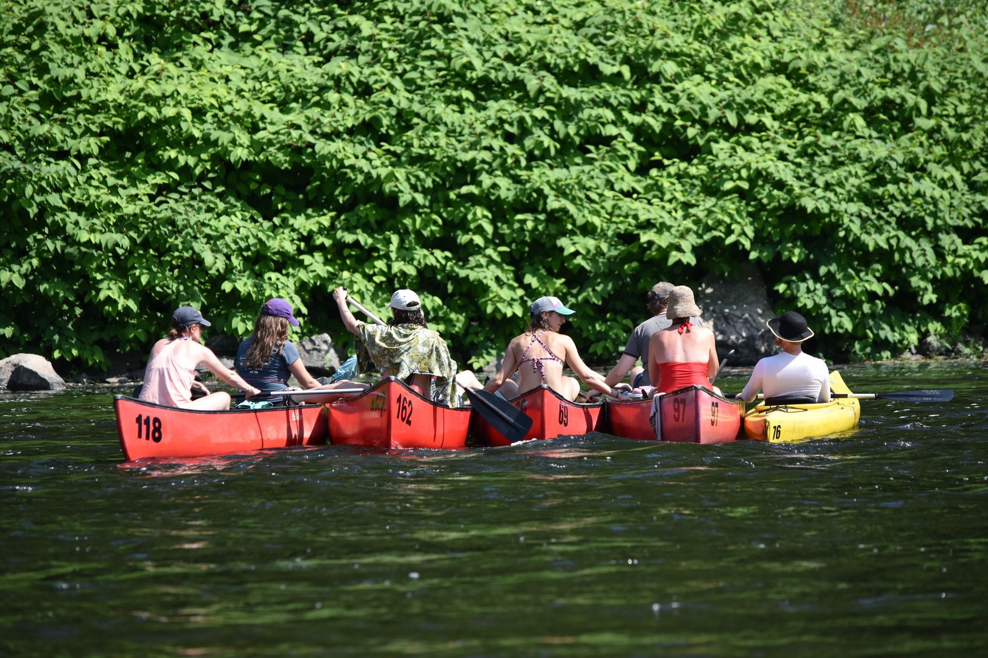 A group from adventure sports are in red canoes on a river.