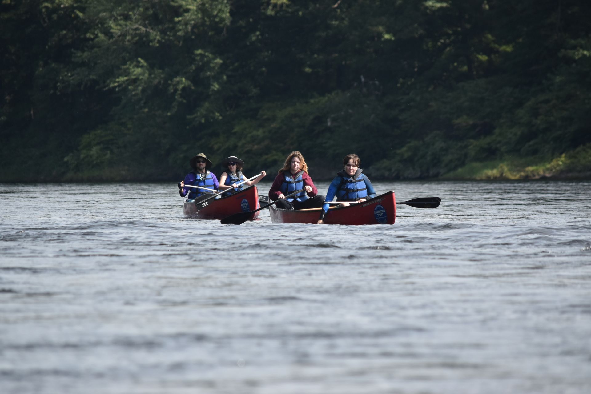 A group of people are rowing in adventure sports canoes down a river.