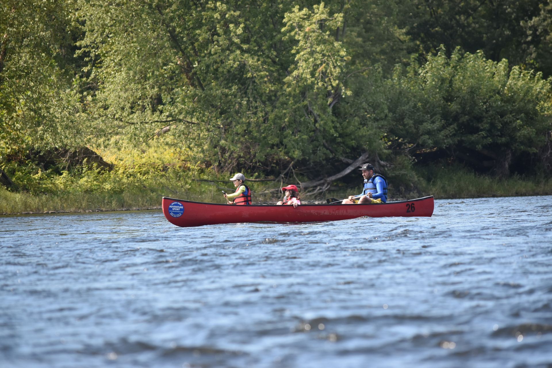 Two people are fishing in a red adventure sports canoe on a lake.