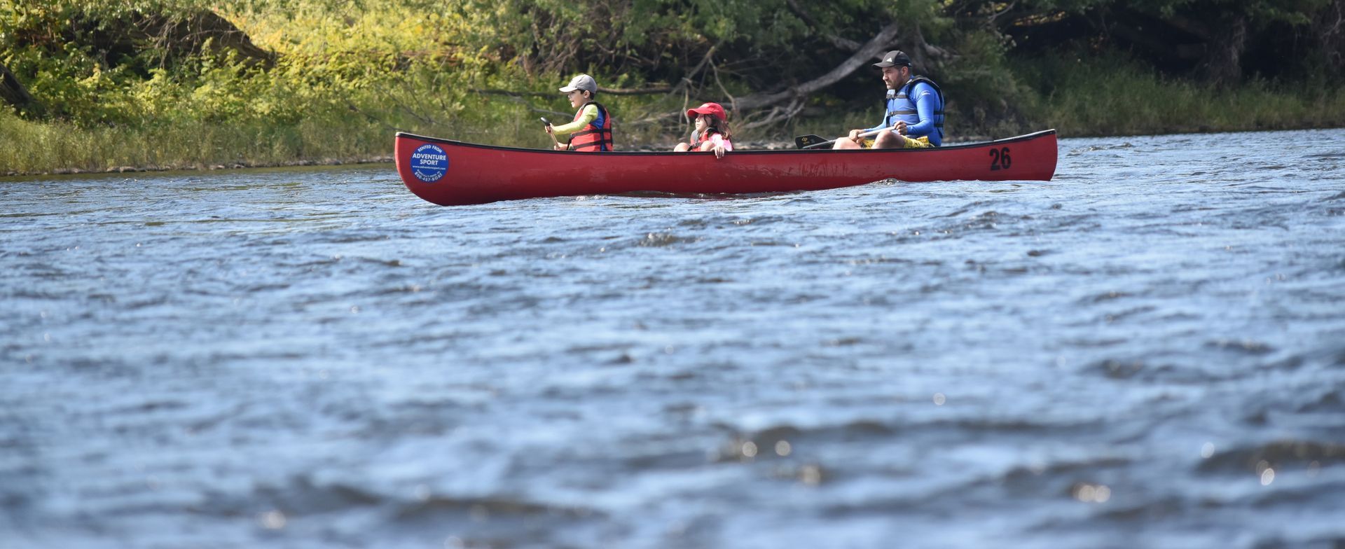 A group of people are in a red adventure sports canoe on a lake.