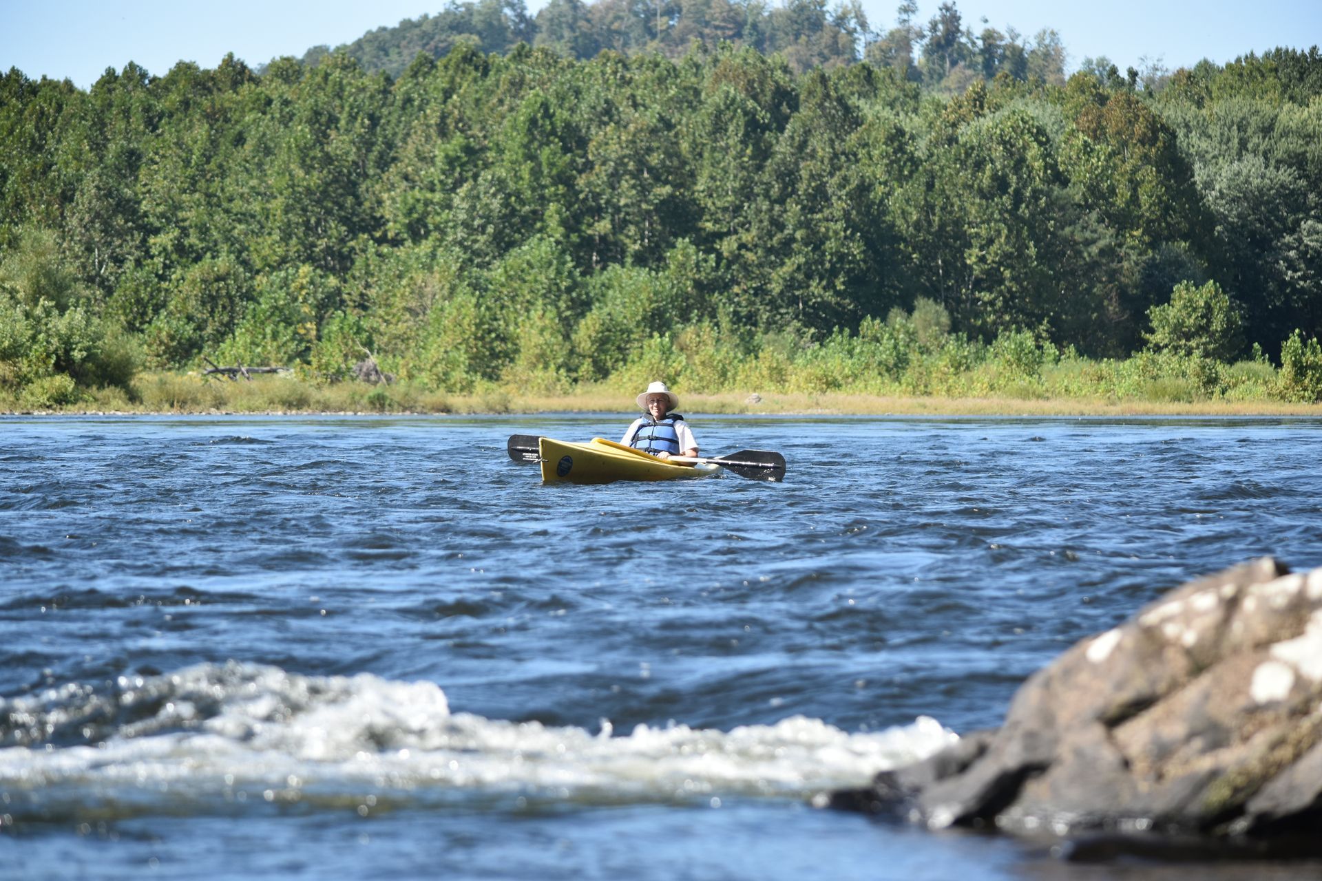 A man in a yellow adventure sports kayak is paddling down a river.