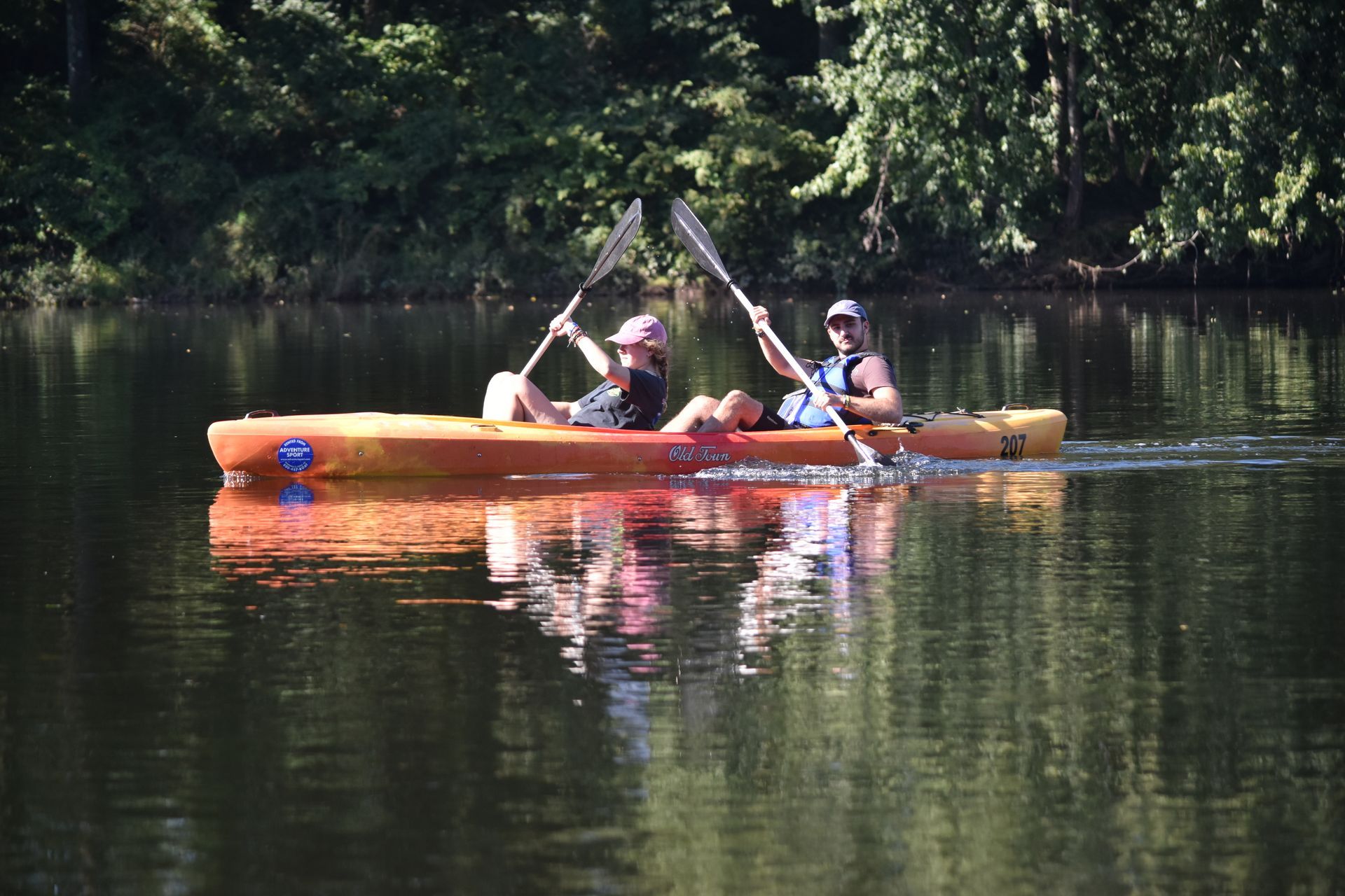 Two people are paddling adventure sports kayaks on a lake.