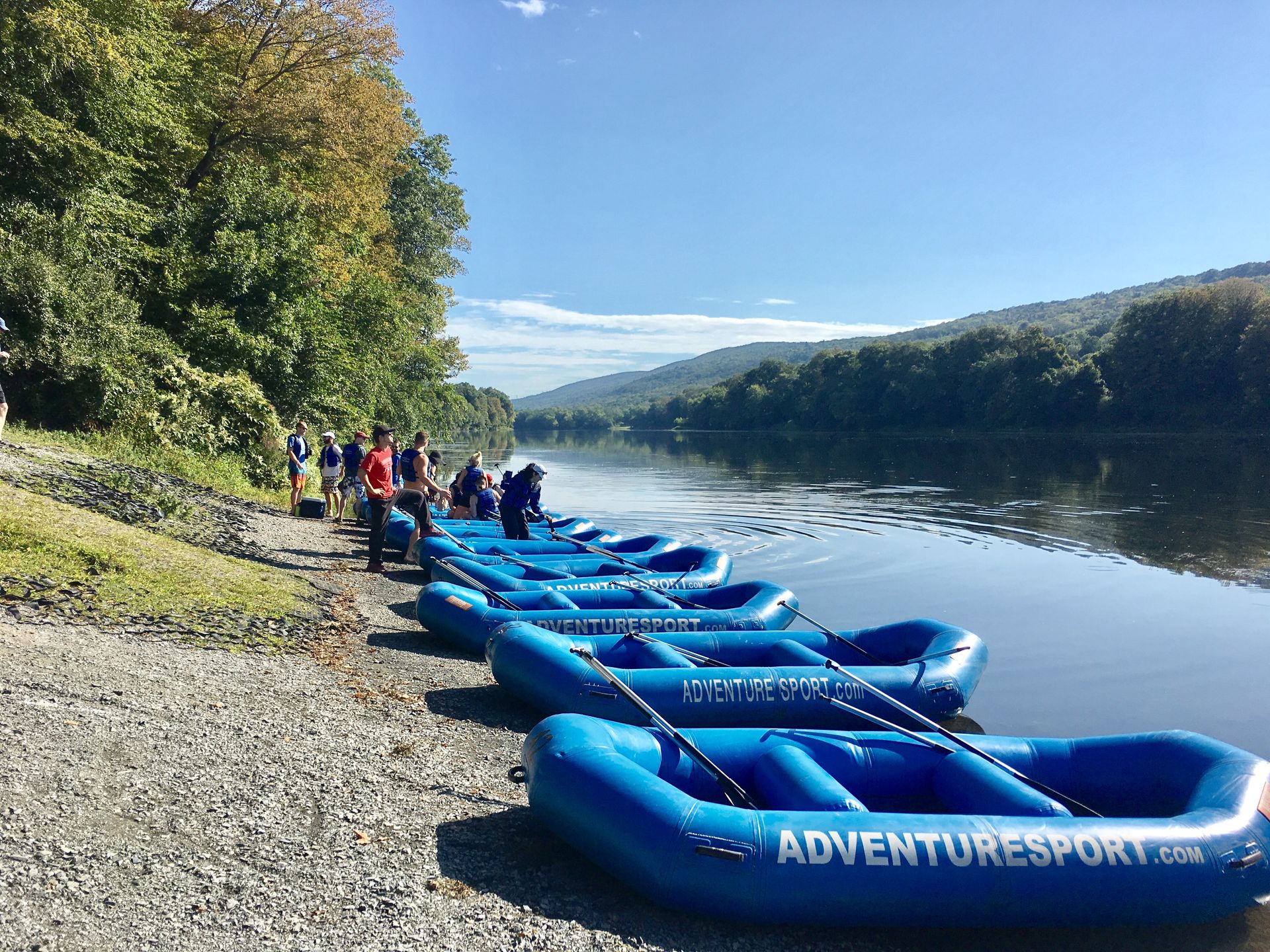 A row of blue adventure sports rafts are lined up on the shore of a river.