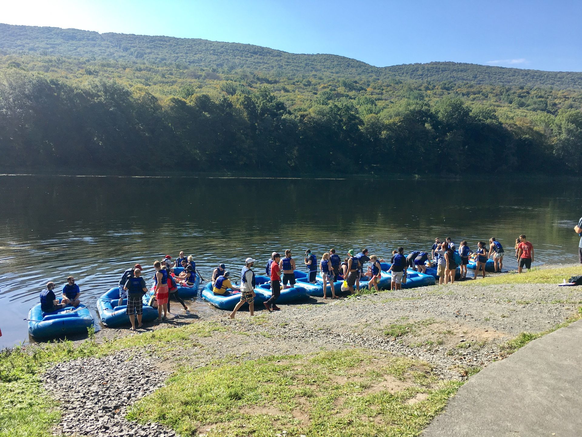 A group of people are standing next to adventure sports rafts on the shore of a lake.