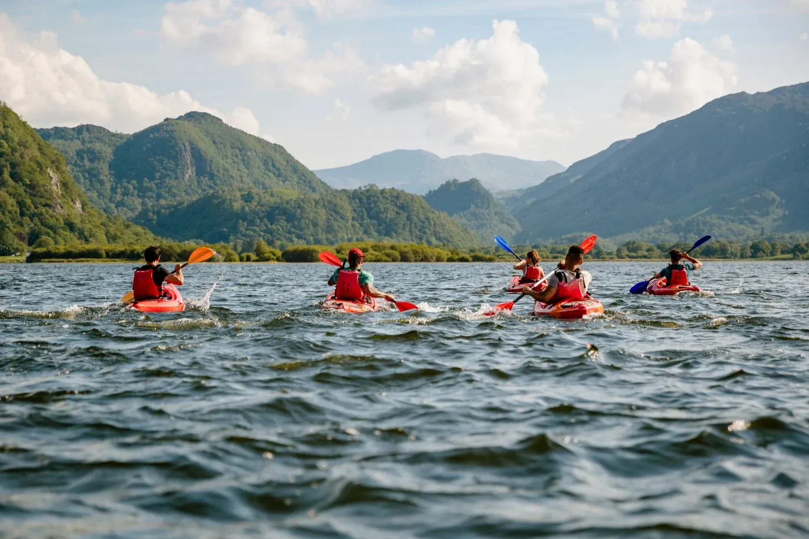 A group of people are kayaking on a lake with mountains in the background.