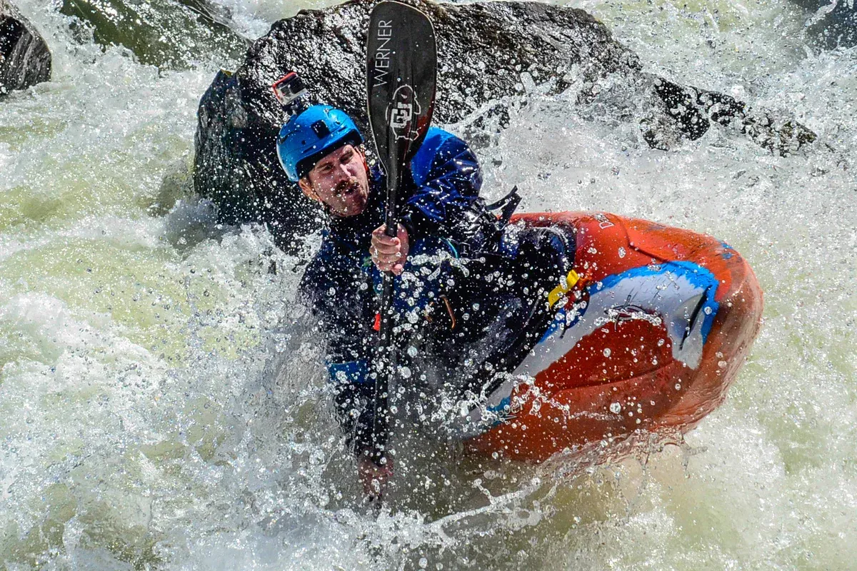 A man is riding a kayak through a river wearing his safety helmet.