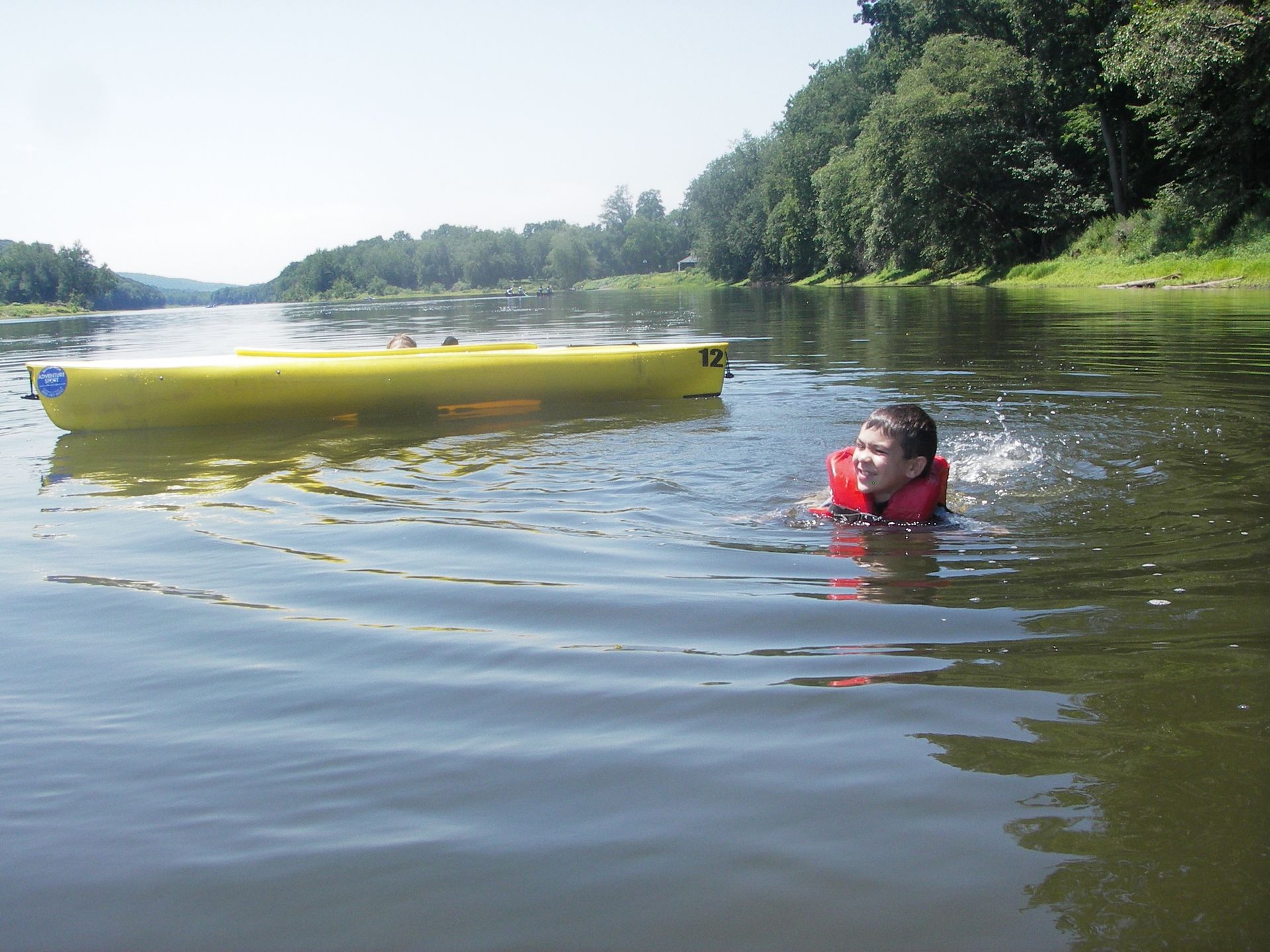 A person  at adventure sports in a life jacket is swimming in a river next to a yellow kayak