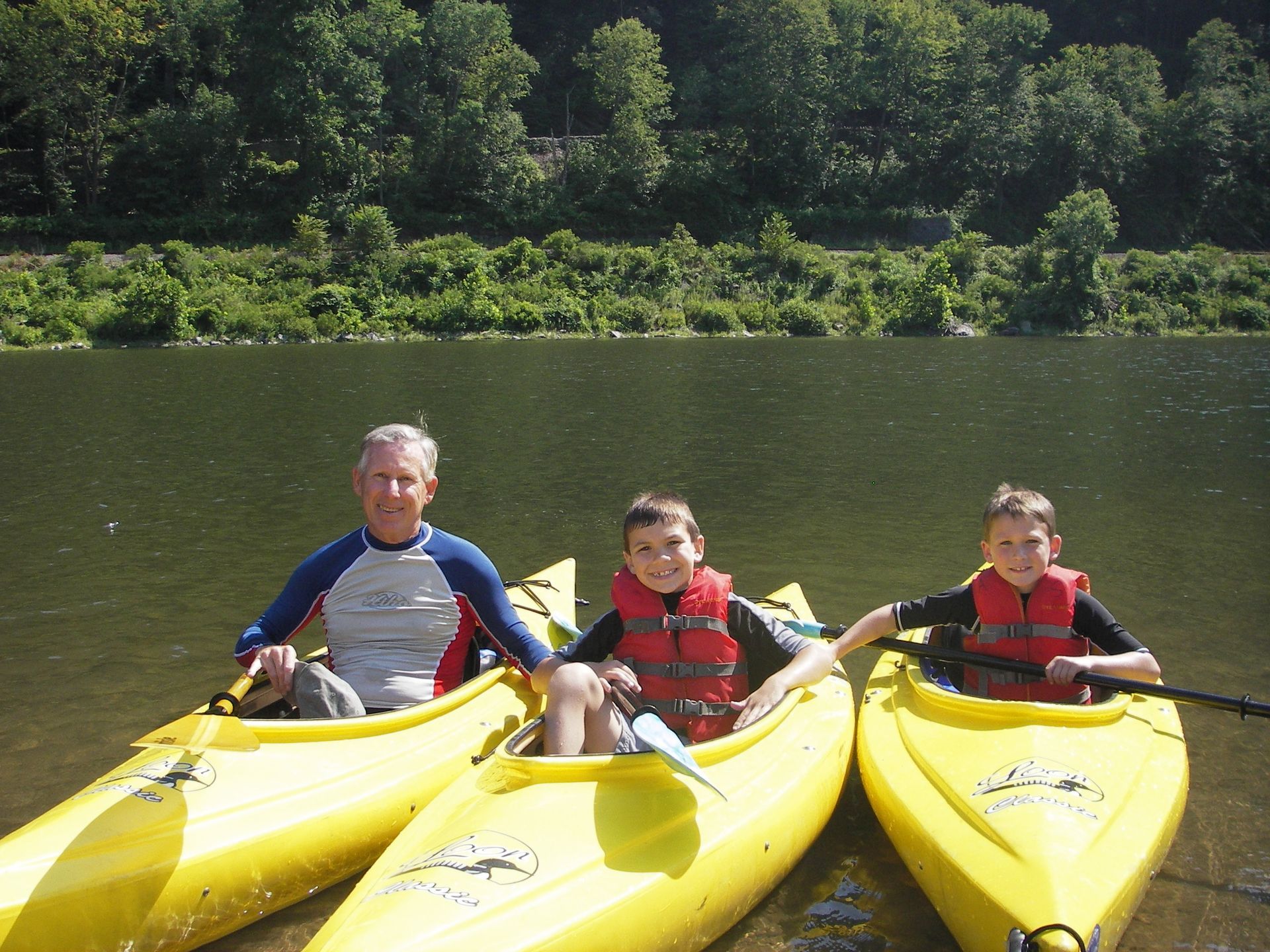 A man and two boys in yellow adventure sports kayaks on a lake