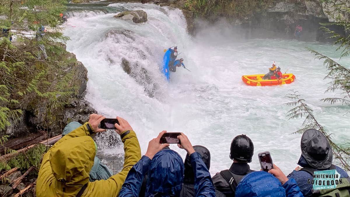 A group of people are taking pictures of a person in a raft in a river.