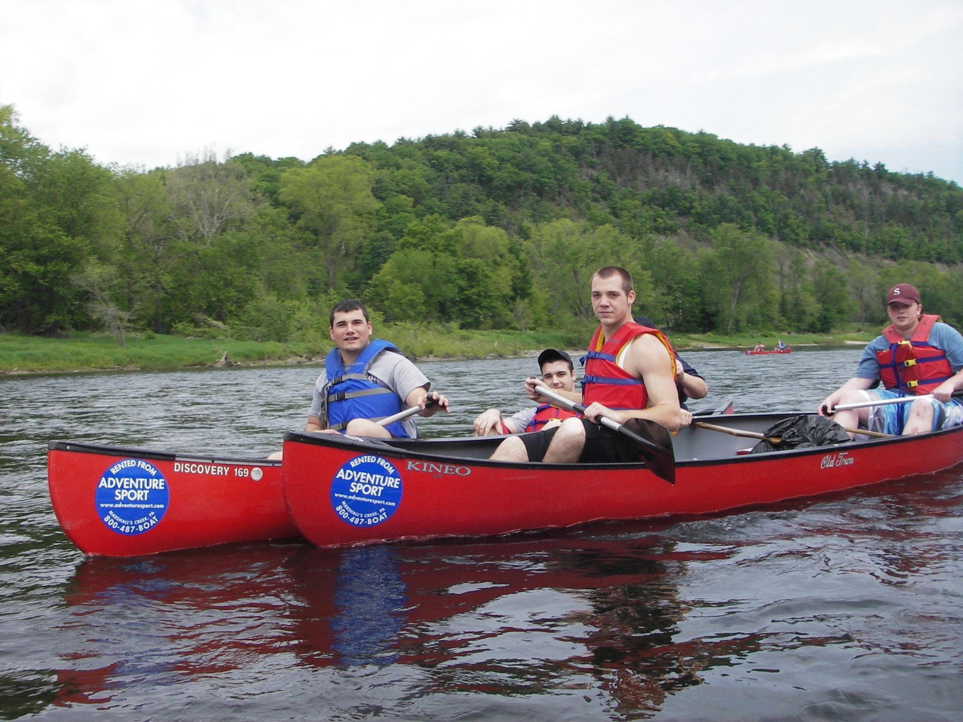 A group of men are in two red adventure sports canoes on a river