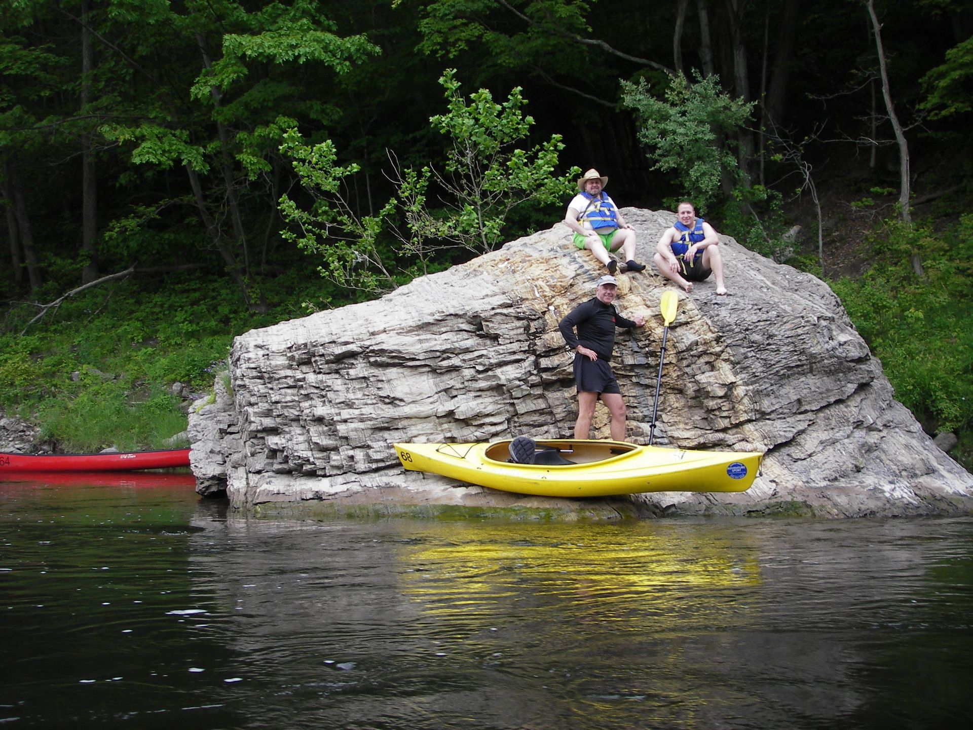 Two men are sitting on a rock next to a yellow adventure sports kayak.