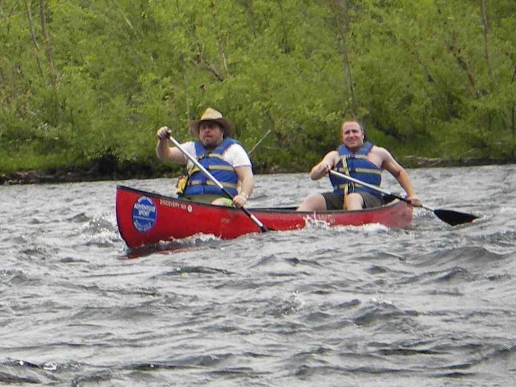 Two people are paddling a red adventure sports canoe on a river