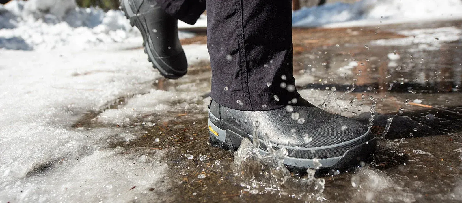 A person wearing black river boots is walking through a puddle of water.