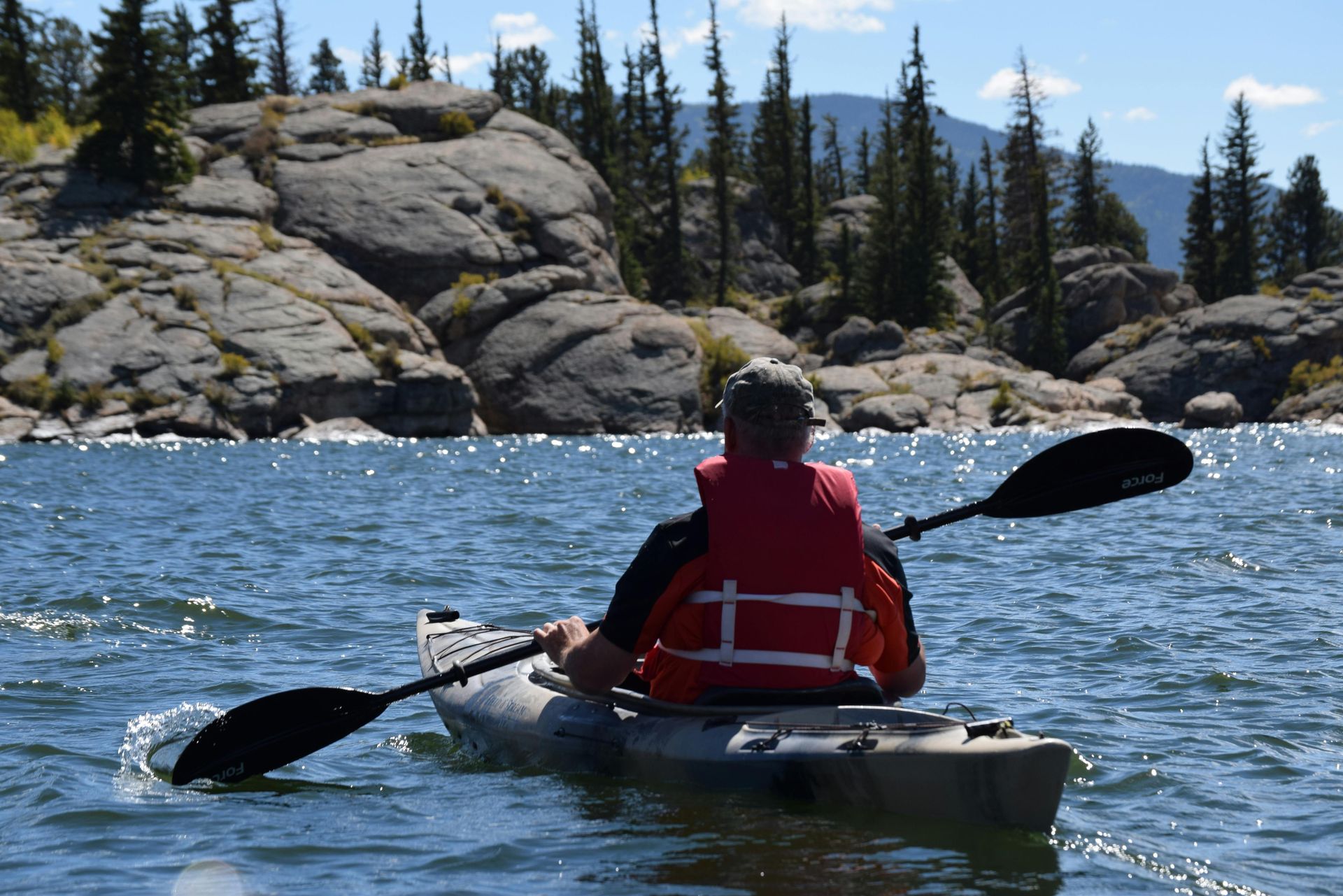 A man in a red vest is paddling a kayak on a lake