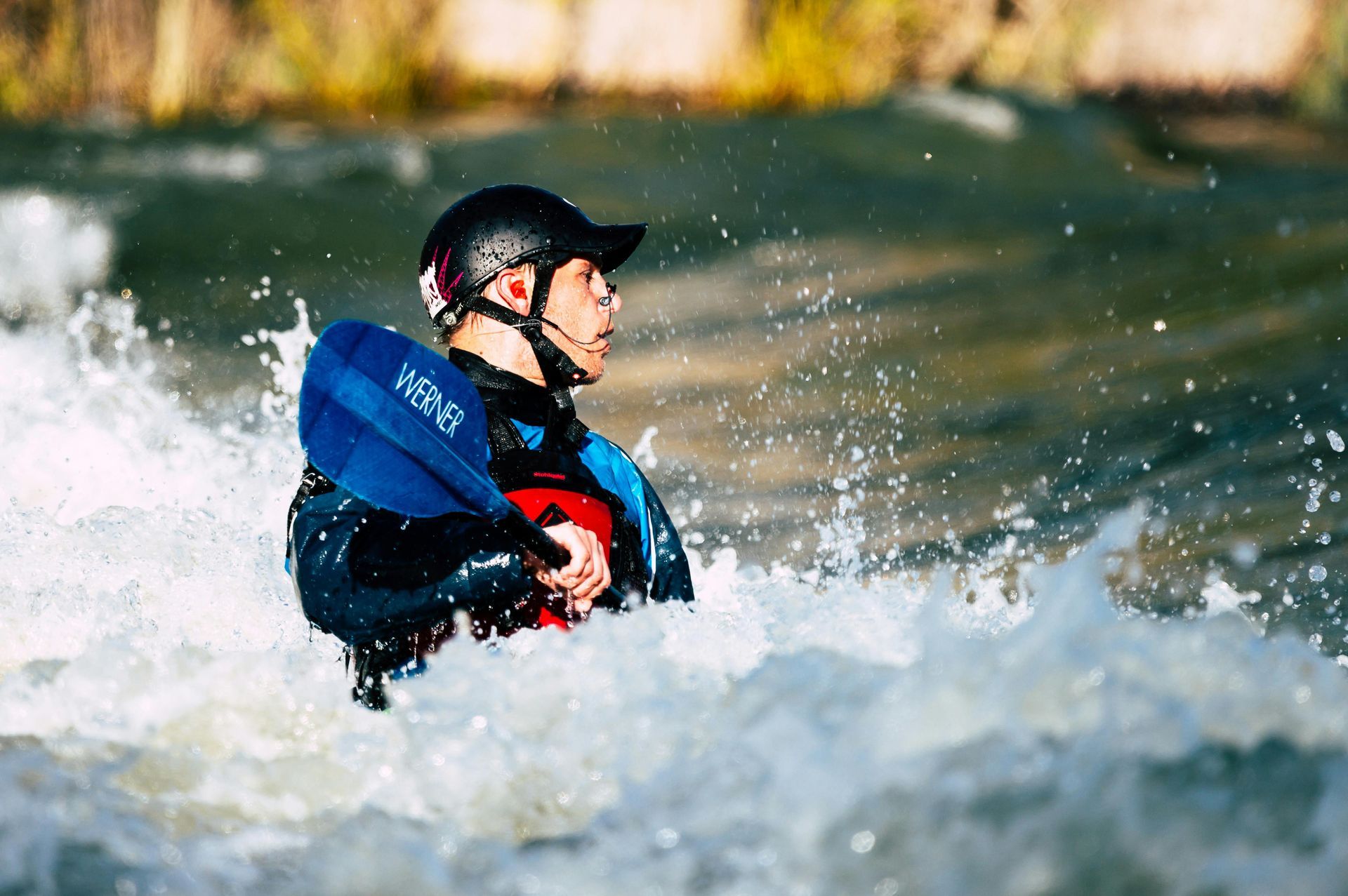 A man in a life jacket is riding a wave in a river.