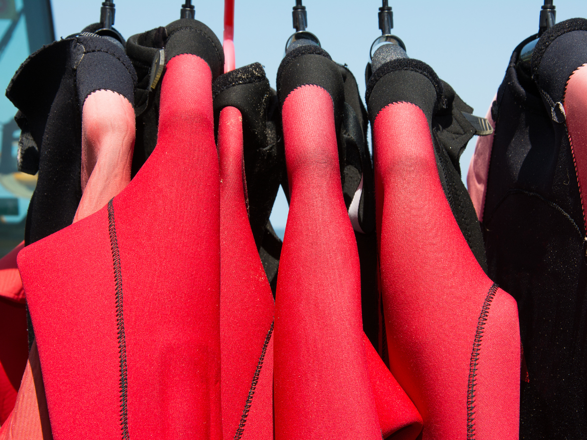 A bunch of red and black wet suits hanging on a rack
