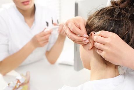 Audiólogo ajustando un audífono a una joven en un centro médico. Un médico sostiene el equipo.